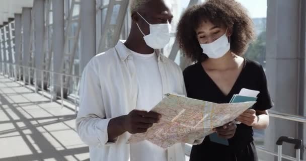 Les jeunes mariés afro-américains couple de personnes se tiennent ensemble portant des masques médicaux de protection contre le coronavirus sur leur visage, en regardant la carte de la nouvelle ville à la recherche d'un moyen de maquillage itinéraire, concept touristique — Video