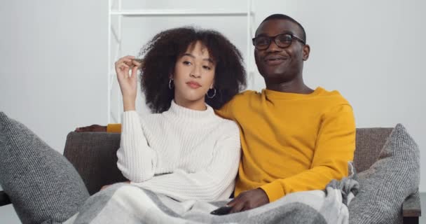 Mulher afro-americana insatisfeita menina étnica sentada no sofá com seu marido homem negro sorridente sentindo tédio, cara mudando canais para TV mudando filme do programa. Família jovem descansando em casa — Vídeo de Stock