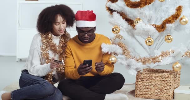 Gözlüklü, Noel Baba şapkalı ve kıvırcık saçlı çift yeni yılı evde kutluyor. İnternet mağazası kuryesinden hediye paketi alıyor. İçinde Noel hediyesi olan bir kutu alıyor. — Stok video