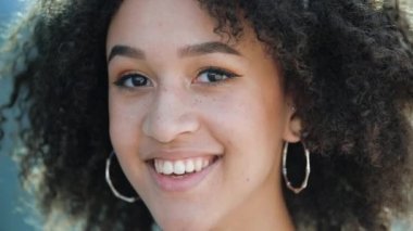 Kendine güvenen güzel bir Afrikalı kadın gülüyor. Mutlu etnik Amerikalı öğrenci kız çilli, kıvırcık saçlı, sağlıklı beyaz dişlerle gülümseyen. Tatmin olmuş bir bayan kameraya doğru bakıyor.