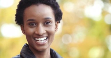 Afro-Amerikan portresi karışık ırk siyahi kadın genç bayan etnik eş açık havada, dişleri açık, neşeli bir yüz ifadesi ile kameraya bakarak gülümsüyor.