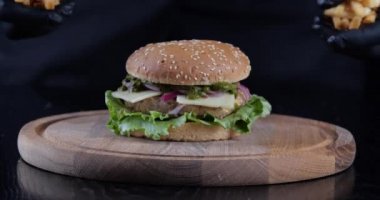 Ahşap tahtada etli büyük hamburgerin yakın çekimi, siyah lateks eldivenli erkek elleri, şef lokanta barında servis etmek için peynirli burgerin yanına çıtır çıtır sarı patates kızartması koyar.