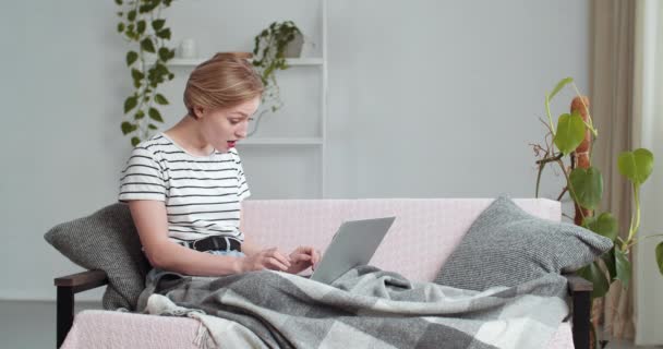 Giovane studentessa caucasica freelance donna guardando computer portatile leggere buone notizie divertenti e-mail ride denti sorridenti guarda la fotocamera seduta sul divano a casa in soggiorno coperto di coperta — Video Stock