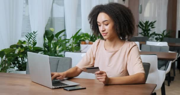 Portret van duizendjarige vrouw Afrikaanse Amerikaanse zakenvrouw zit in cafe restaurant maakt gebruik van laptop om te kopen in online winkel maakt orde houdt credit bank plastic kaart in haar handen, concept van korting — Stockvideo