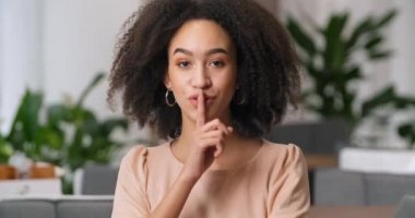 Yakın plan portre Afro-Amerikan kıvırcık saçlı güzel kız parmaklarını ağıza koyuyor. Sessiz hareket işareti gösteriyor. Gizli bilgi dedikodu işareti konuşmayı yasaklıyor.