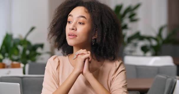 Close-up vooraanzicht van pensive vrouwelijk gezicht, portret van afro-Amerikaanse krullende millennial bezoeker dame zitten in cafe restaurant met gevouwen handen in de buurt van haar kin te wachten om eten te bestellen kijkt uit raam — Stockvideo