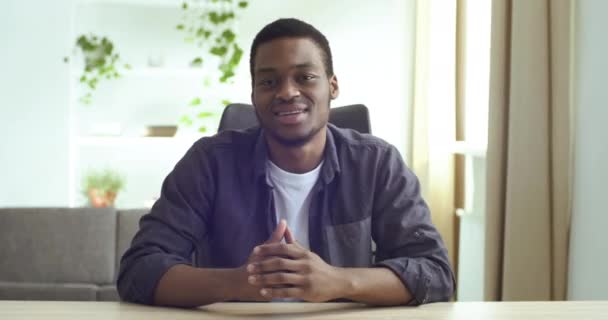 Visa från webbkamera afro Amerikansk ung vänlig kille sitter vid bordet hemma på kontoret talar berättar information genomför lektion online chatta med vänner på distans under karantän av pandemiskt virus — Stockvideo