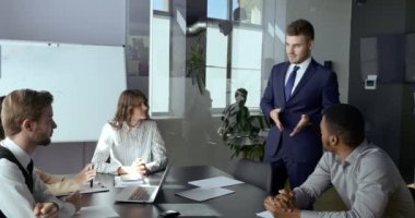 Çok ırklı, çok ırklı iş adamları profesyonel yöneticilerden oluşan bir ekip. Kafkas erkek lider meslektaşlarının önünde duruyor ve proje ortaklarının sonuçları hakkında konuşuyor