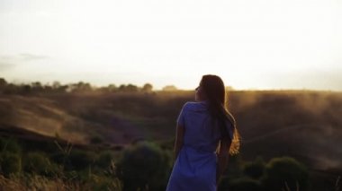 Çekici Avrupalı kız, akşam güneşi altında çimlerin üzerinde uzun saçlarını sallıyor. Genç ve mutlu bir kadın doğada vakit geçirmekten ve eğlenmekten hoşlanır..