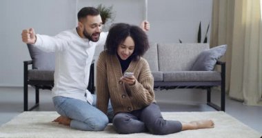 Karışık ırklar arası ilişki. Çok ırklı bir aile yerde oturmuş cep telefonlarının online video kliplerine bakıyorlar. Sosyal ağda sohbet ediyorlar.