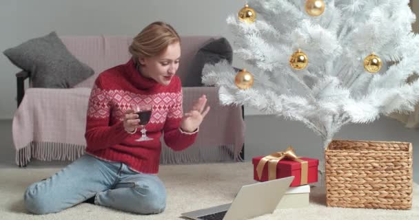 Привлекательная счастливая девушка кавказская женщина сидит дома на карантине самоизоляции из-за эпидемии коронавируса празднует Новый год в одиночестве размахивая рукой, здороваясь на ноутбуке веб-камера делает видеозвонок — стоковое видео