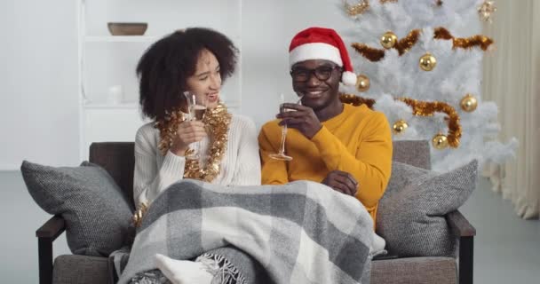 Happy afro american couple clink champagne glasses toast and celebrate together New 2021 Year at home in living room sitting against glowing Christmas tree, holiday party. Congratulations concept — Stock videók