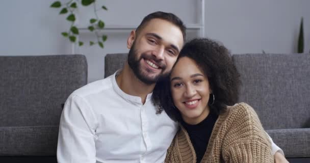 Interracial relationship, portrait of young people close-up male and female face afro american girlfriend and caucasian boyfriend sitting hugged cuddled looking at camera smiling toothy family concept — Wideo stockowe