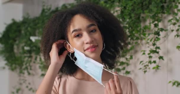 Portrait of afro american girl black woman putting on medical mask on face protects her mouth and nose from respiratory virus bacteria shows sign of approval like puts thumb up, life during pandemic — Vídeo de stock