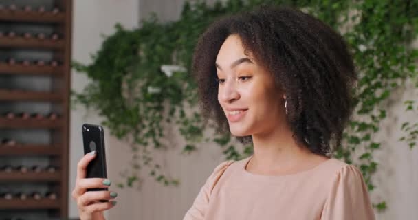 Ritratto di Afro American amichevole ragazza nera giovane donna che tiene il telefono in mano guarda lo schermo parla alla fotocamera web del dispositivo mobile comunica con gli amici del marito in remoto tramite video chat — Video Stock