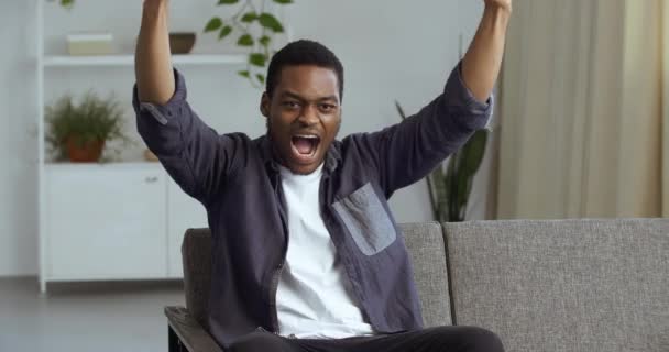 Happy moment, guy student african american man cheering for his favorite team shouting raises his hands up saying wow supports enjoying game emotionally reacting to winning port competition on tv home — Video Stock