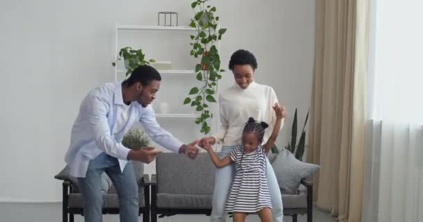 Щасливий безтурботний активний афро-американська етнічна пара танцює з милою дошкільною дочкою маленьких дітей дочка у вітальні в домашньому інтер'єрі разом, батьки сім'ї з дитиною вихідні веселий рух — стокове відео