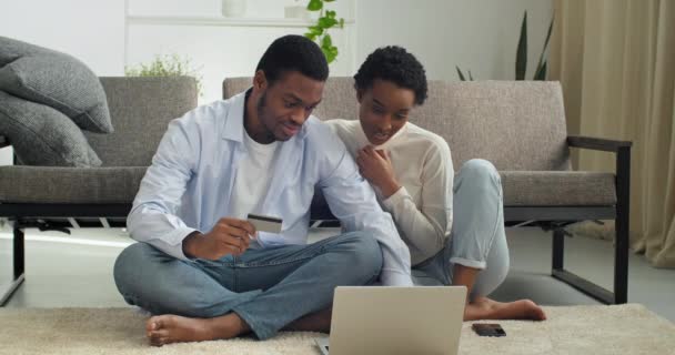 Young black man holding credit banking card payment information with focused smiled millennial afro american woman doing online shopping order, happy couple involved in purchasing goods in internet — Αρχείο Βίντεο