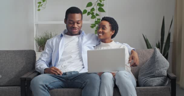 Afrikanisch-amerikanisches Paar frischvermählte Mann und Frau Bruder und Schwester sitzen zusammen auf dem Sofa im Wohnzimmer mit Laptop reden zu Hause diskutieren Entscheidung, neue Möbel online kaufen wählen — Stockvideo