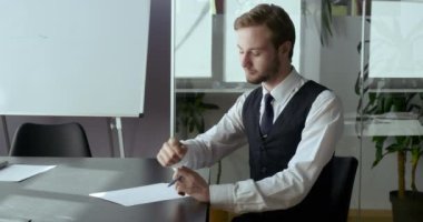 Modern ofis evinde masa başında oturan Kafkasyalı iş adamı lideri onaylama onay sembolü olan kamera karşısında başparmaklarını kaldırarak zaferin sembolünü gösteriyor. Kağıt kaleme gülücük gibi yazılar yazıyor.