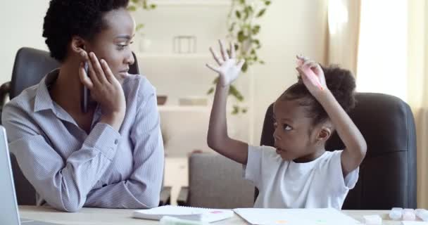 Retrato de mujer afroamericana con el pelo corto se sienta en la mesa en casa o en la escuela con su hija estudiante negro escribir dibujo con bolígrafos y marcadores en papel en el cuaderno comunicar hablar hablar — Vídeo de stock