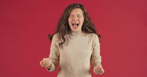 Blank jong vrouw tiener meisje staat poseren op rode achtergrond in studio geschreeuw opent haar mond en luid schreeuwt zwaaien haar handen van woede hondsdolheid concept van woede problemen overbelasting stress — Stockvideo