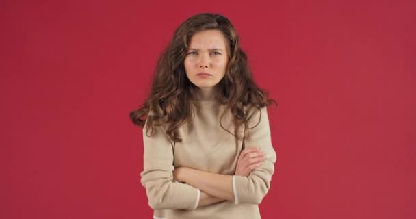 Sad offended woman millennial caucasian girl teenager crosses her arms makes displeased face frowns eyebrows feels angry rage misunderstanding, concept of problems, studio portrait on red background — Stock Video