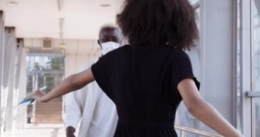 Kıvırcık saçlı, siyah elbiseli, siyah elbiseli genç Afro-Amerikalı kadın, etnik yakışıklı adamla tanışmak için yalanıyor, tıbbi maskeli çift havaalanında buluşuyor, karantina sırasında seyahat ediyor.