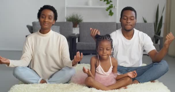 Ruhige afro-amerikanische Familie Mutter Vater und Tochter zu dritt sitzen auf dem Boden in Lotusposition meditieren zusammen loszuwerden Stress Spannung Yoga-Übung entwickeln spirituell geistig achtsames Lebenskonzept — Stockvideo