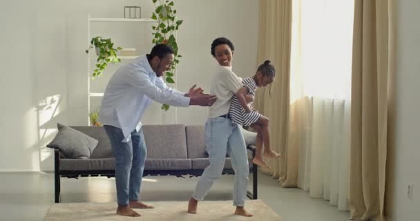 Genç afro amerikan ebeveynler kısa saçlı güzel anne ve siyah adam baba evde çocuğuyla vakit geçiriyorlar kızlarını kollarında tutuyorlar ve bebek bebekle oynuyorlar, aile sevgisi kavramı — Stok video