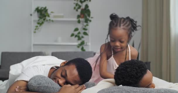 Retrato familiar de família afro-americana pais jovens dormindo no sofá na sala de estar relaxante após o dia difícil bonito filha saltar impede a mãe e o pai de relaxar faz barulho, conceito infantil impertinente — Vídeo de Stock