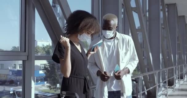Счастливая афро-американская этническая пара в медицинских защитных масках радоваться поездка отпраздновать поездку отпуск чувствовать радость открытия границ стоять вместе на терминале аэропорта во время пандемии коронавизуса — стоковое видео
