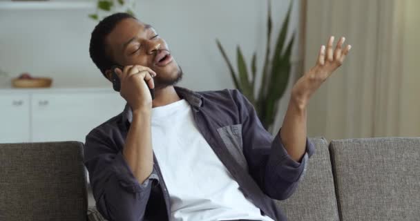 Afro americano ragazzo conduce un'intervista per telefono parla su smartphone con colleghi, amici di famiglia o con ragazza discute informazioni, conduce il dialogo a distanza da casa seduta sul divano — Video Stock