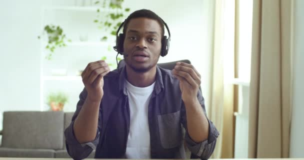 Webcam vue de l'enseignant afro-américain, employé de bureau porte un casque et un microphone, conseille les clients en ligne à distance pendant la quarantaine du coronavirus et la pandémie. Jeune homme étude à la maison — Video