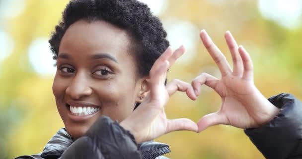 Usmívající se milující upřímný africký Američan dívka černošky žena ukazuje ruce gesto lásky symbol podpory a sympatie symbol záhyby prsty do tvaru srdce stojí izolované venku, romantika koncept — Stock video