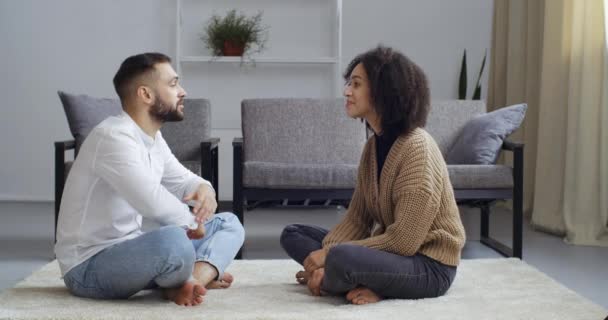 Interracial couple afro-américain femme et caucasien mari parler assis sur le sol en position lotus discuter rêver souriant, gars nettoie les ordures de filles sweat-shirt, concept de soins d'amour — Video