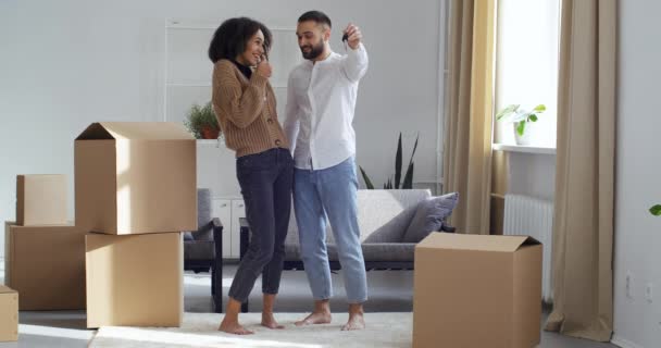Young caucasian man caring happy confident proud husband showing afro american woman black girl wife keys to new house standing together surrounded by cardboard boxes with things, real estate purchase — Stock Video