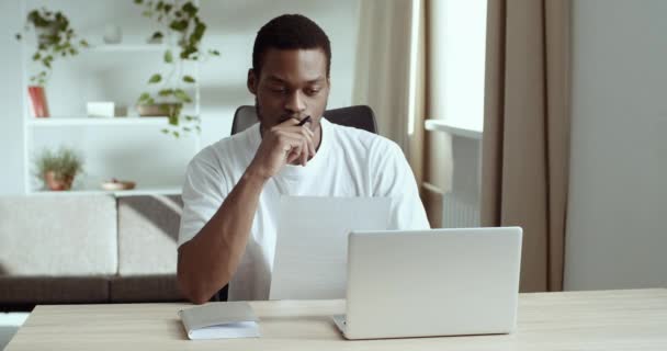 Сконцентрированный задумчивый чернокожий бизнесмен афро-американец журналист читает документ, делая бумажную работу пишет идеи, делая заметки, изучая удаленно сидя за столом автора сочиняя роман — стоковое видео