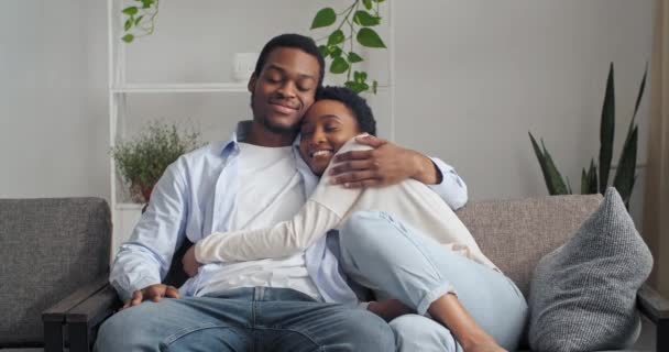 Sorrindo casal feliz homem negro e mulher americana africana menina com abraço de cabelo curto enquanto sentado no sofá em casa na sala de estar desfrutando de tempo juntos descansando aconchego, amor e conceito de apoio — Vídeo de Stock