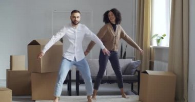 Genç insanlar, iki yeni evli çift müziğe aktifçe dans ediyor. Yeni evdeki kutularla çevrili el ve ayaklarıyla senkronize hareketler yapıyorlar. Gayrimenkul satın alma kavramı.