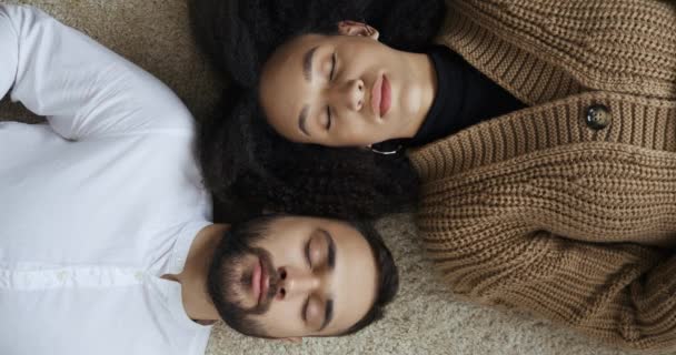 Young multiethnic couple afro american woman and caucasian man teenagers in love lying on floor after work day trying to relieve stress and relax sleep wake up open eyes look at the camera top view — Stock Video