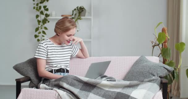 Donna caucasica seduta sul divano a casa sotto coperta termina la conversazione in video chat conferenza online agitando la mano facendo gesto di addio alla webcam del computer portatile, concetto di comunicazione remota — Video Stock