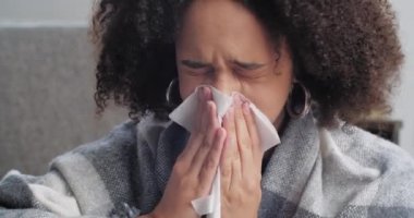 Afro-Amerikalı kızın burun akıntısı, grip virüsü belirtileri, kağıt peçeteye üfleyen yün battaniyeyle kaplanmış bir kadın evde oturan ısıyı hissediyor.
