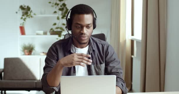 Serious Afro American male student studying remotely communicates with teacher taking exam on video online chat conference sitting at home, business person working advises clients on head microphone — Stock Video
