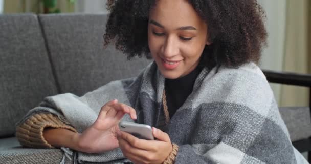 Retrato de mulher afro-americana menina étnica conversando enquanto sentado em casa no chão coberto com cobertor de lã olha para a tela do telefone da mensagem de digitação gadget moderna on-line se comunica com os amigos — Vídeo de Stock