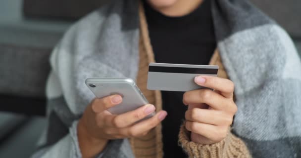 Close-up mujer de piel oscura chica joven en suéter envuelto en cuadros manos femeninas sostener el teléfono móvil utiliza un gadget moderno y tarjeta bancaria de crédito hace la compra en línea, e-commerce concepto de negocio electrónico — Vídeos de Stock