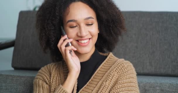 Afro amerikansk kvinna etnisk flicka talar på mobiltelefon hemma vila kommunicera med vänner lär sig goda nyheter svar samtal chatta med pojkvän eller familj sitter på soffan hemma — Stockvideo