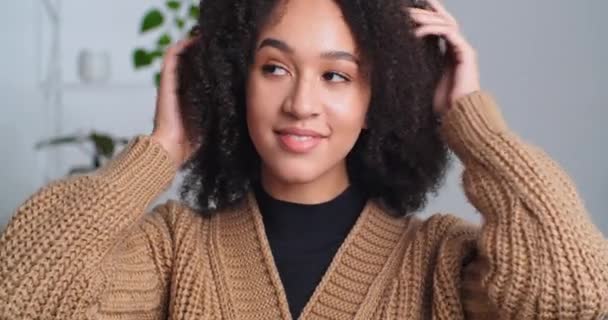 Porträt einer Frau Modell afroamerikanische Mädchen richtet lockiges Haar berührt Frisur mit ihren Händen genießt Styling Malerei sitzt im Schönheitssalon sieht kokett in die Kamera, Mode-Stil-Konzept — Stockvideo