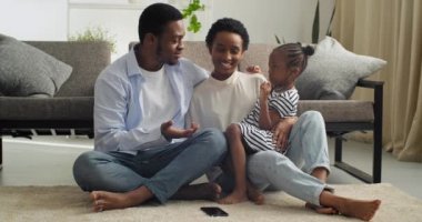 Üç çıplak ayaklı çift, bebek Afro-Amerikan aile babası ve tatlı küçük kız çocuğu yumuşak sıcak halıda oturmuş hafta sonları sohbet ediyorlar.