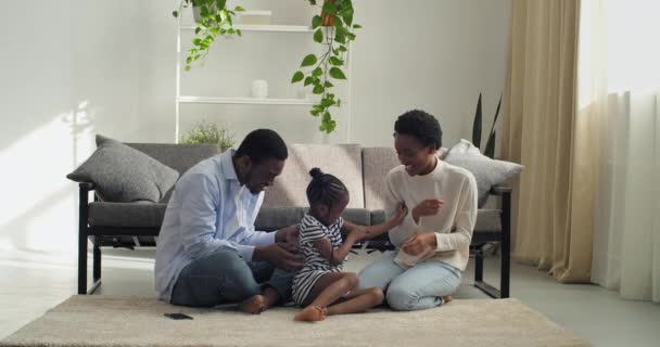 Couple avec enfants parents et jolie fille gaie afro américaine femme et homme mari et femme et fille enfant assis ensemble sur le tapis trois personnes passent du temps ensemble jouer smilling — Video